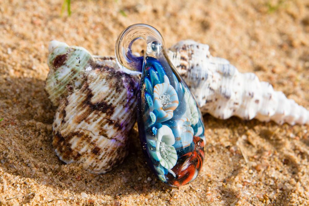 Glass coral reef pendant on sandy beach with blue hues and colorful polyp clusters infused with cremation ashes
