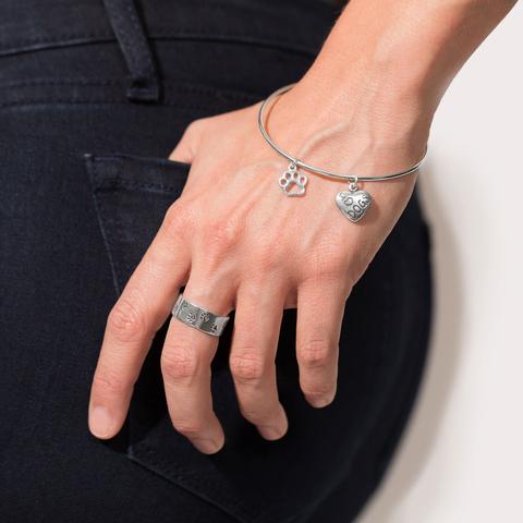 Wrist wearing a silver bracelet with paw print cutout charm and heart charm