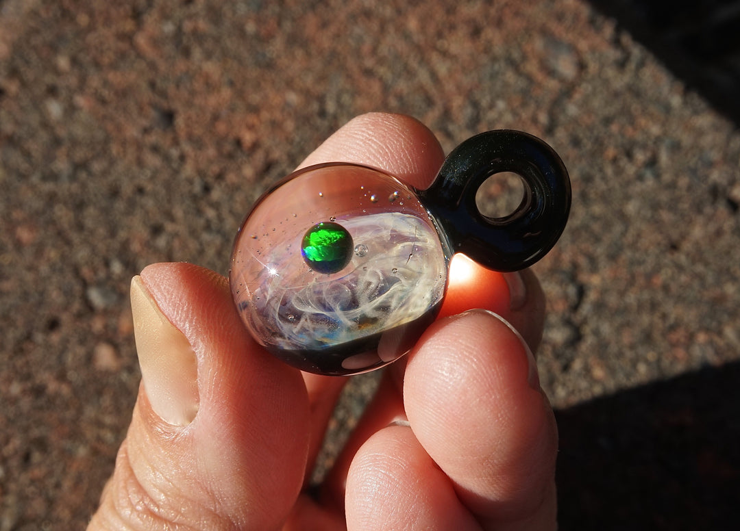 Galaxy style glass planet pendant with a green opal and cremation ashes in swirled clear glass and a black bail