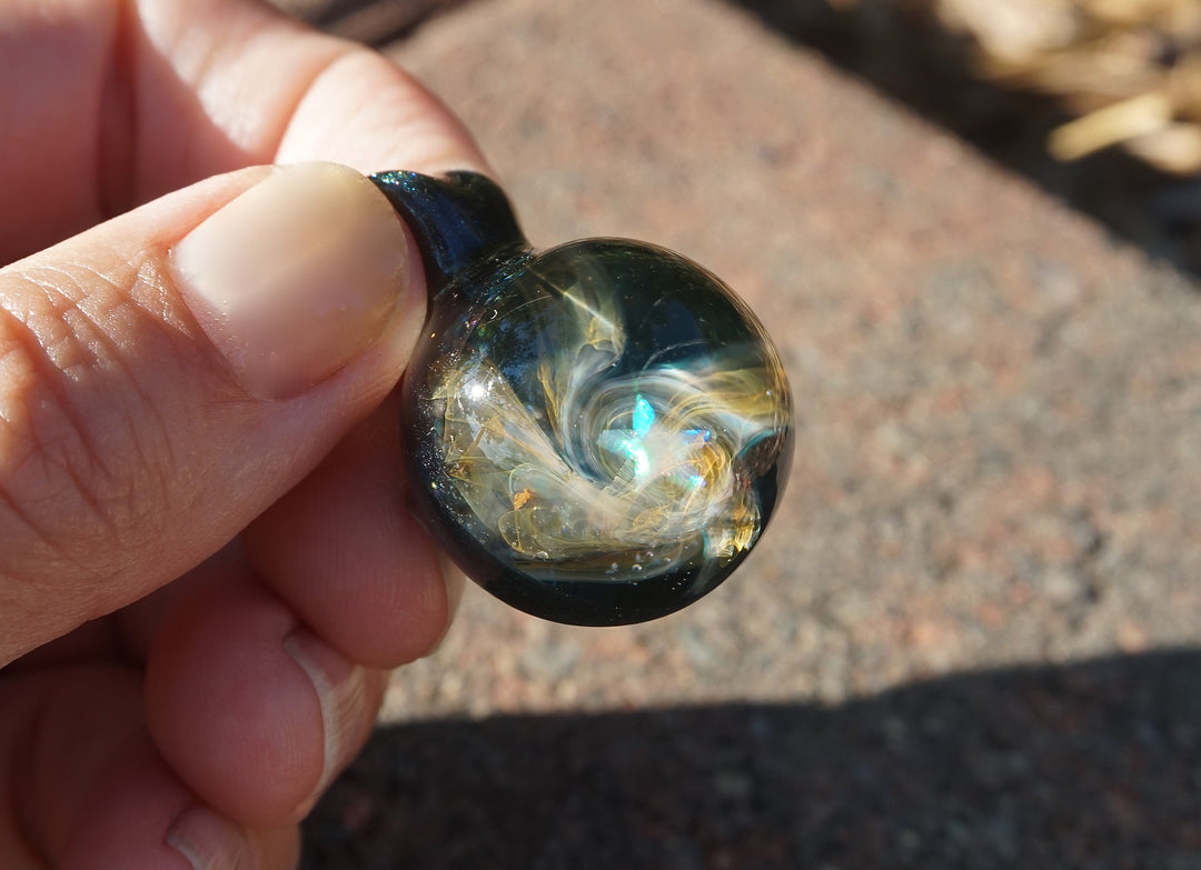 Close up of a round galaxy glass pendant with blue white swirls and an iridescent center stone