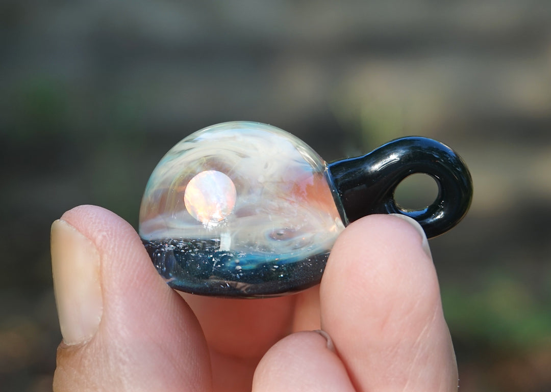 Galaxy style glass planet pendant with a pinkish orb inside swirled glass and a black loop bail