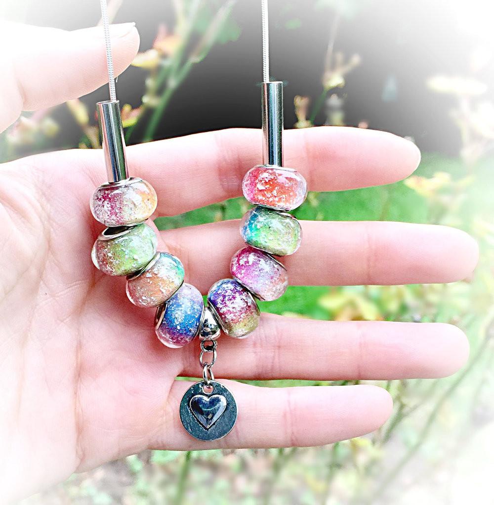 Close up of Rainbow's Bridge necklace with eight rainbow ash beads and a heart charm held in a hand