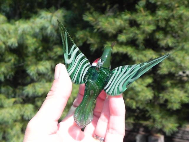 Green glass hummingbird infused with cremation ashes, red throat, striped wings extended, viewed from the side.