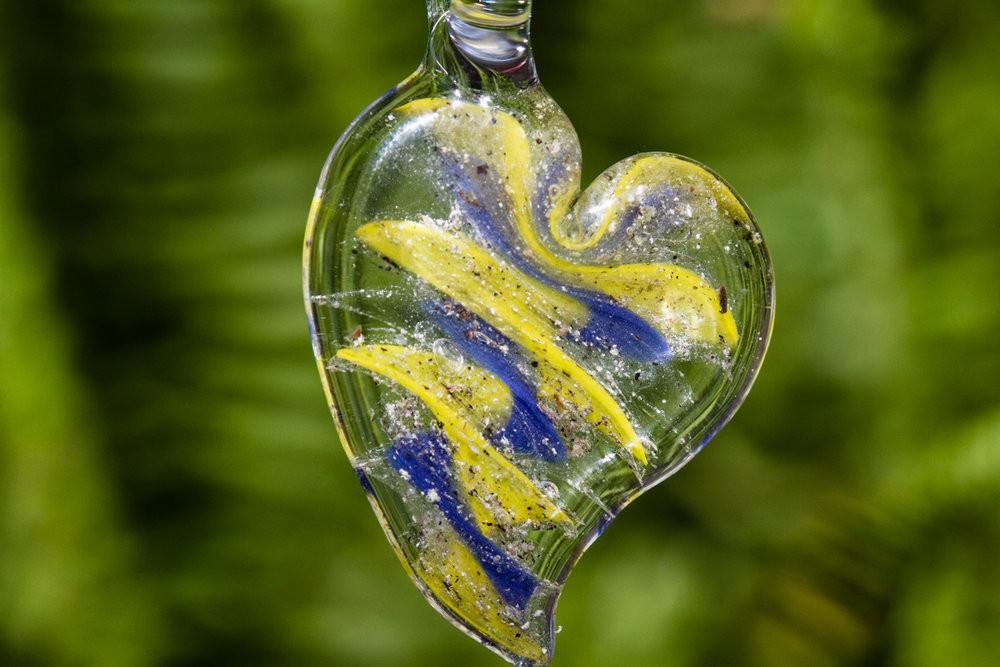 Ripple Heart Necklace pendant infused with cremation ashes in a clear glass heart with blue and yellow swirls on a green background
