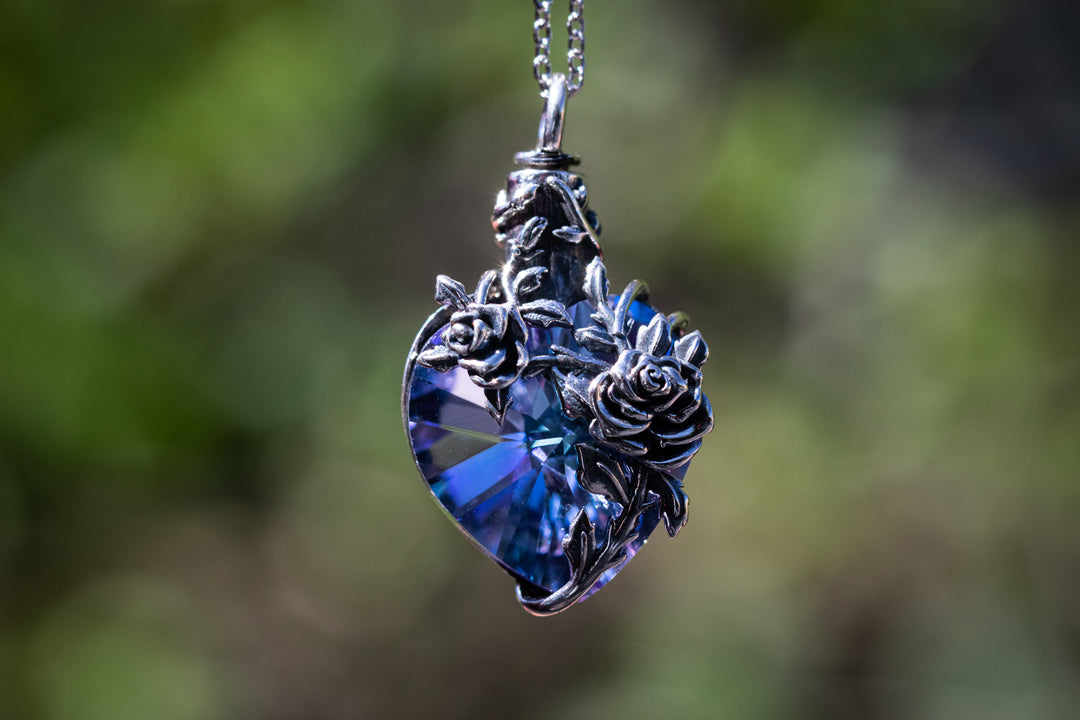 A sterling silver keepsake urn pendant with a blue crystal and floral details, suspended by a chain.