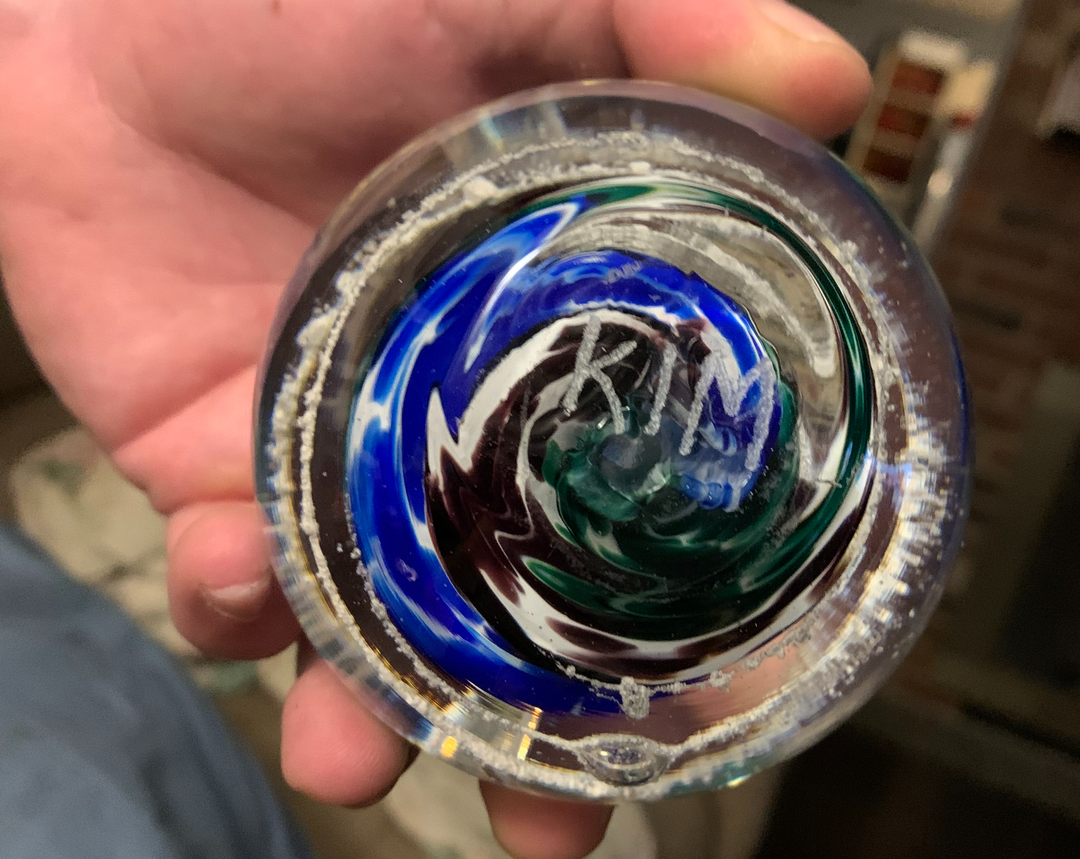 Close up of a swirled glass cremation orb with blue green and red swirls held in a hand.