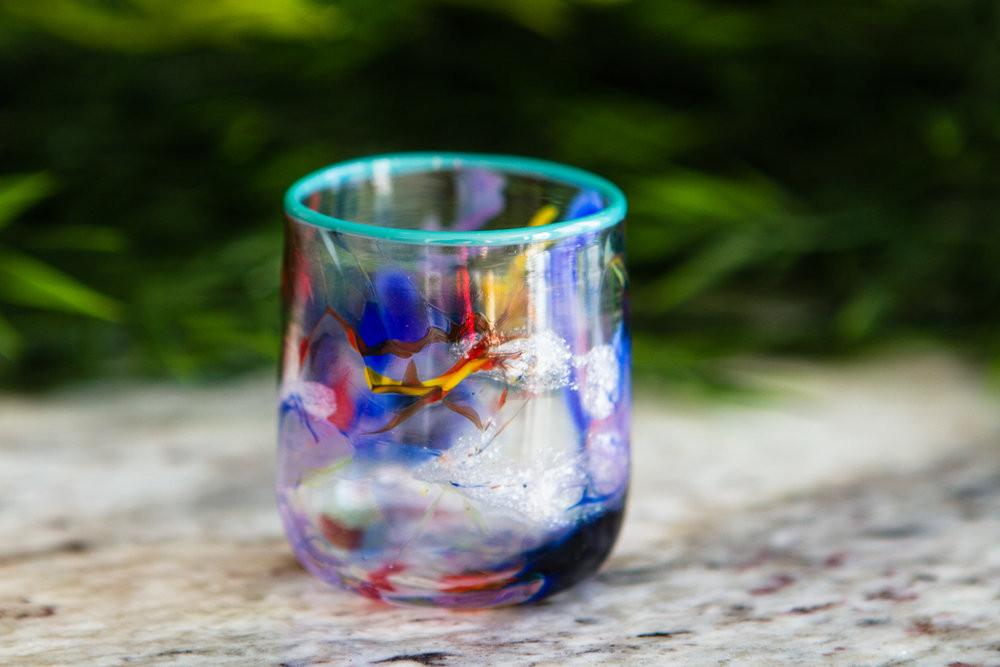 Colorful ash infused glass shot glass with a teal rim and swirling blue and red pigments