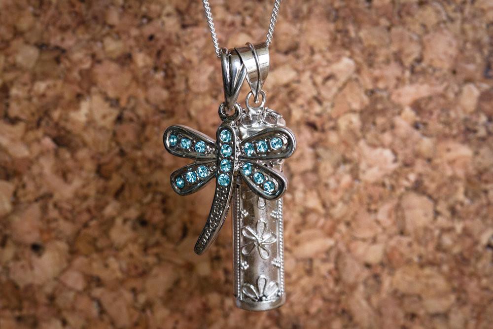 Sterling silver keepsake necklace featuring a daisy motif and a blue crystal dragonfly beside a floral embossed cylindrical keeper.