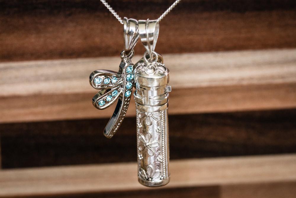 Sterling silver necklace featuring a daisy floral engraved cremation capsule pendant and a blue crystal dragonfly charm.