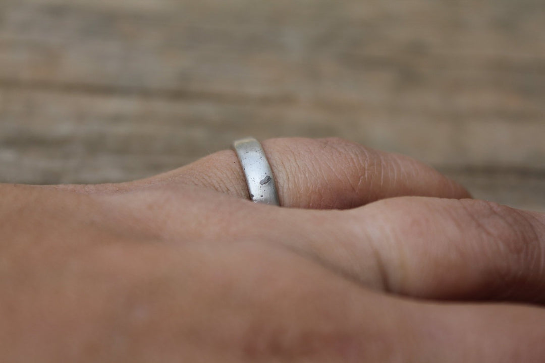Close up of a silver cremation ashes ring worn on a finger.