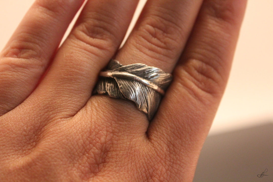 Close up of a sterling silver feather ring worn on the finger, showing carved feather pattern and antiqued finish