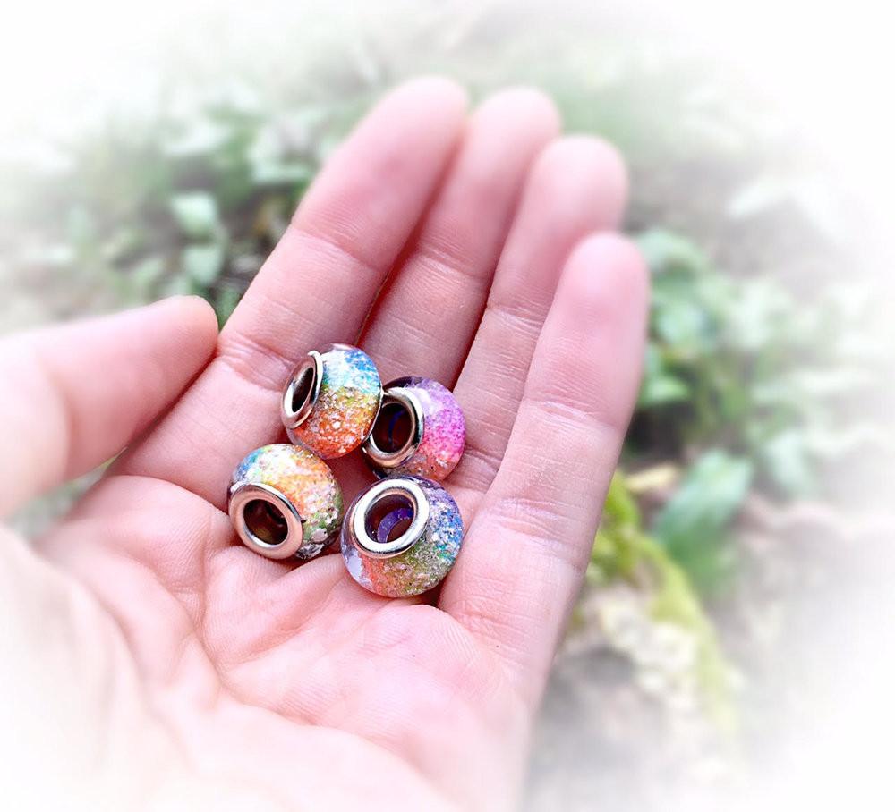 Rainbow cremation ash beads with metal inner holes held in a hand.
