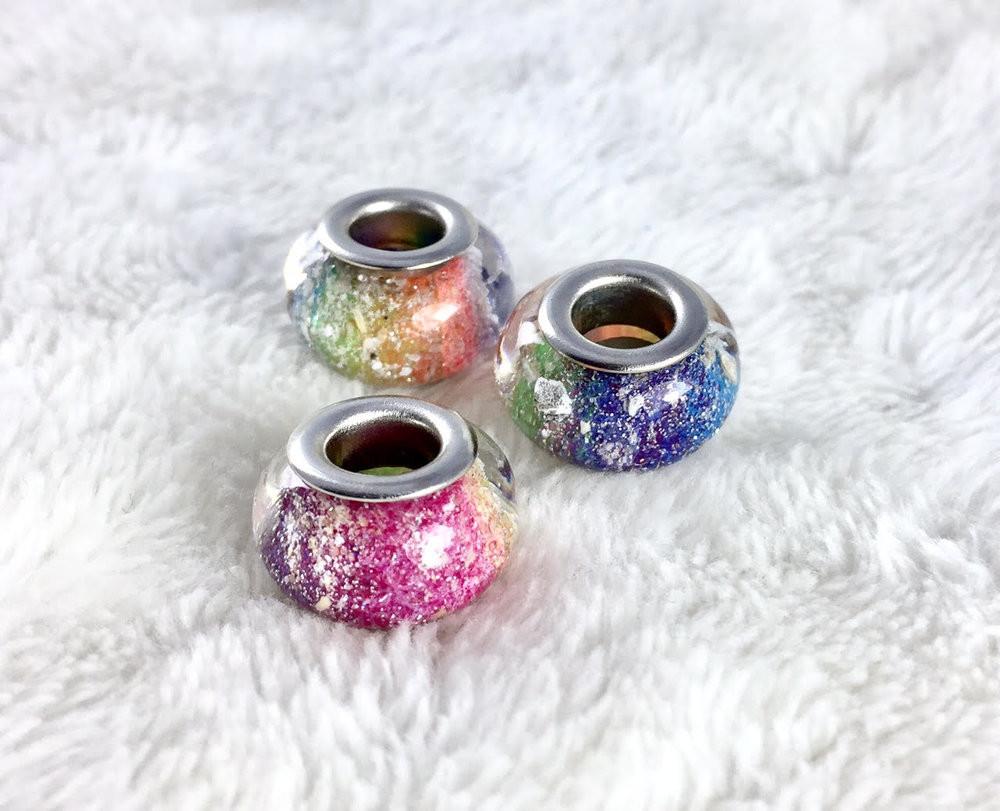 Group of rainbow cremation ash beads on soft white fabric