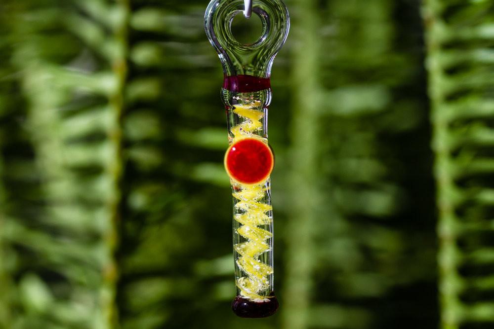 Green glass cross pendant infused with cremation ashes featuring a red accent disc and yellow swirls.