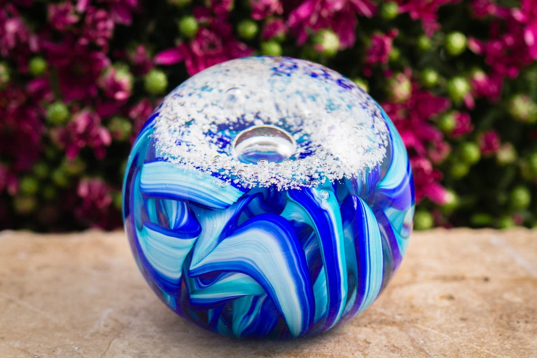 3 inch glass orb with blue white swirls and a frosted snowy cap on a stone surface outdoors