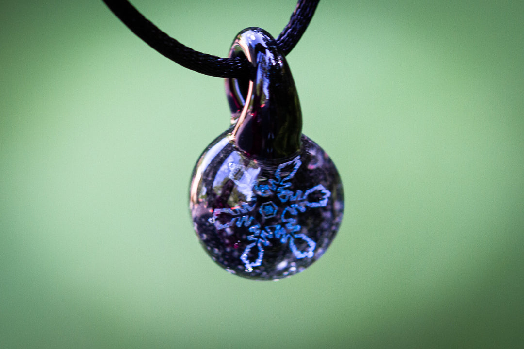 Holographic blue and silver snowflake pendant encased in glass infused with cremation ash, suspended from an adjustable cord.