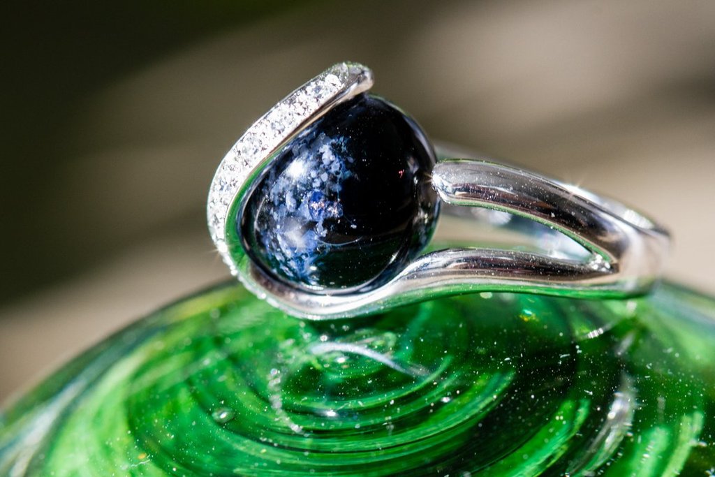 Sterling silver ring featuring a dark blue glass marble infused with cremation ash wrapped by a curved pavé diamond band