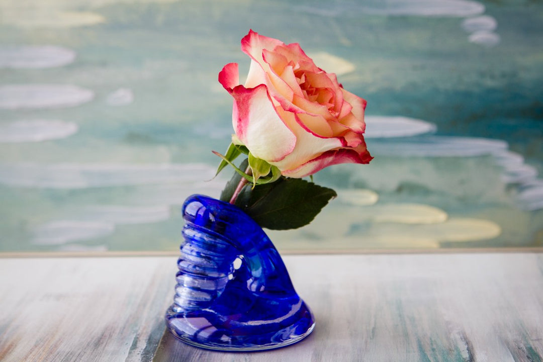 Blue spiral bud vase infused with cremains holding a pink edged white rose on a light marble surface.