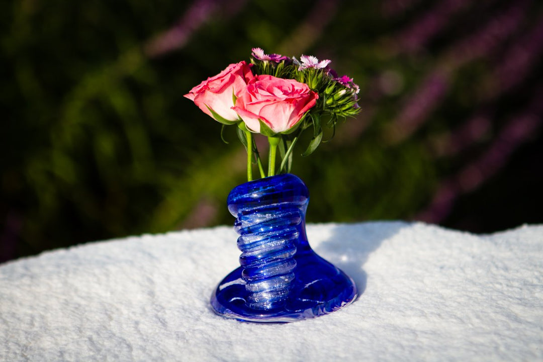 Blue Spiral Bud Vase with cremains supporting pink roses on a snowy surface