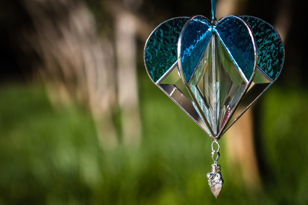 Teal stained glass memorial heart suncatcher with a faceted central diamond and a hanging silver keepsake pendant.