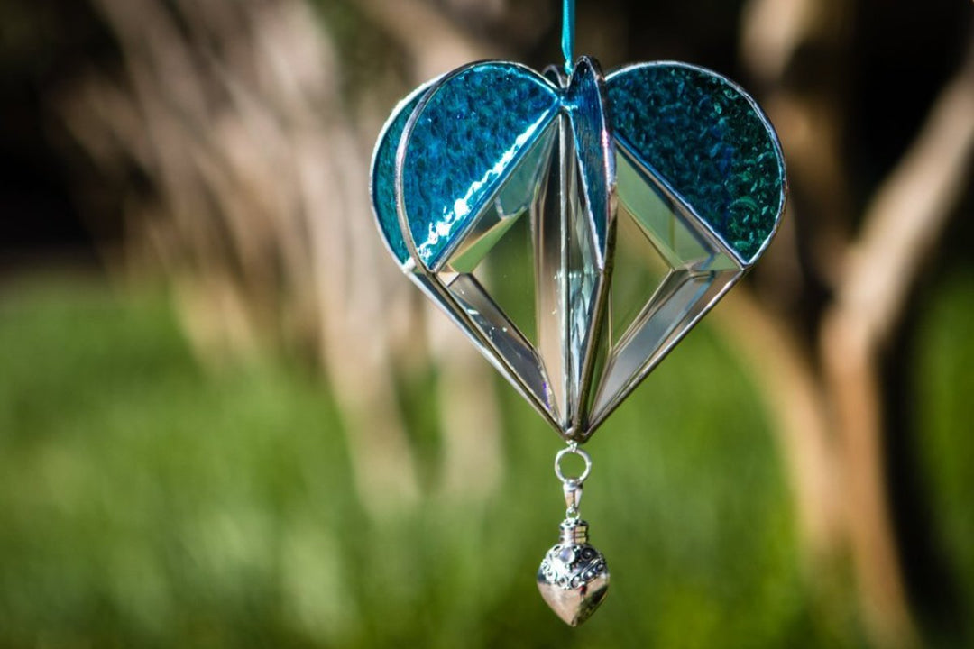 Stained glass memorial heart suncatcher with teal blue panels and a dangling silver heart keepsake pendant.