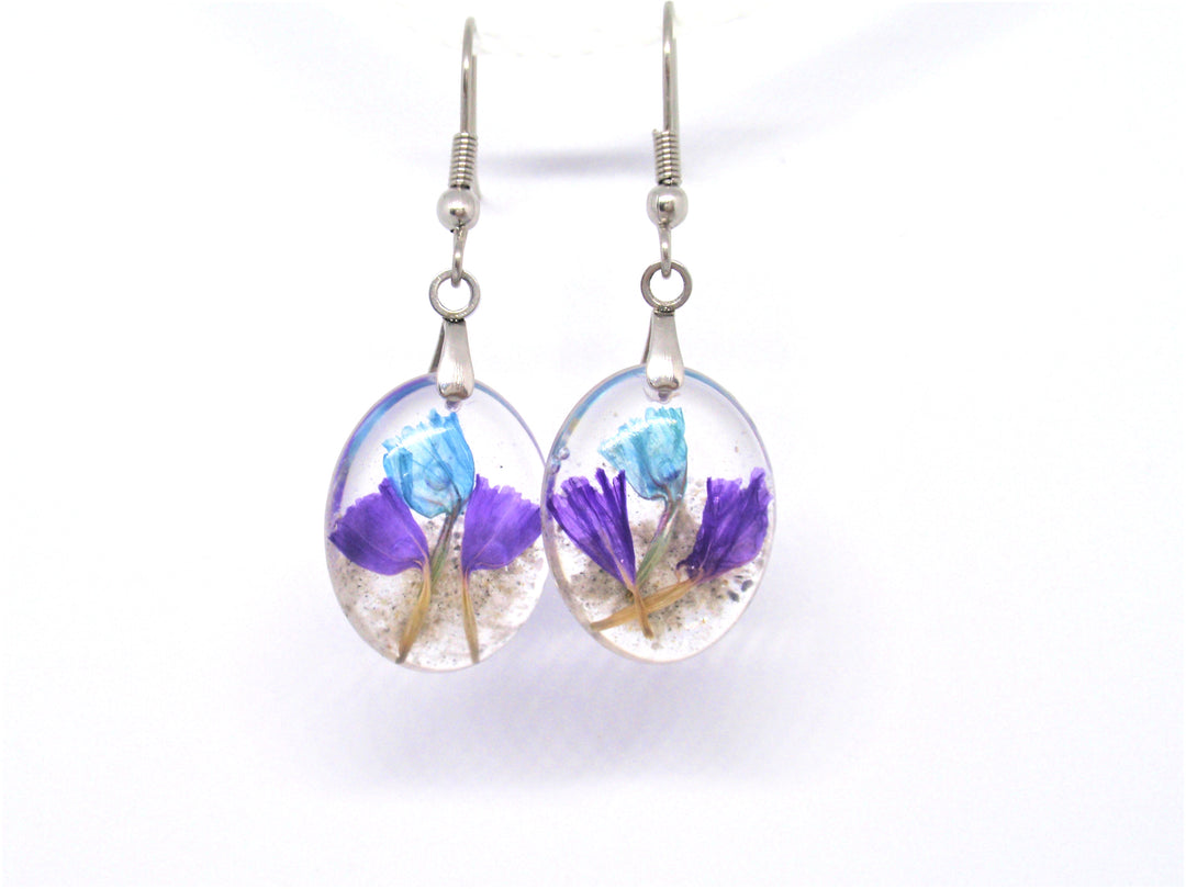 Oval crystal resin earrings containing blue and purple statice flowers with cremains on surgical steel hooks