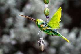 Close up of green glass hummingbird with a silver heart keepsake urn hanging below the beaded strand of turquoise beads.