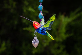 Colorful glass hummingbird pendant with a turquoise beaded strand and a dangling silver heart keepsake urn.