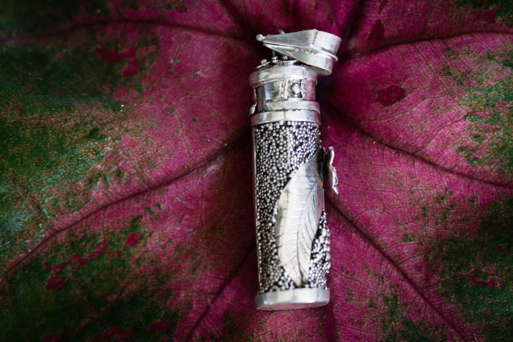 Close up of a silver keepsake pendant with a blooming flower on a textured beaded surface.