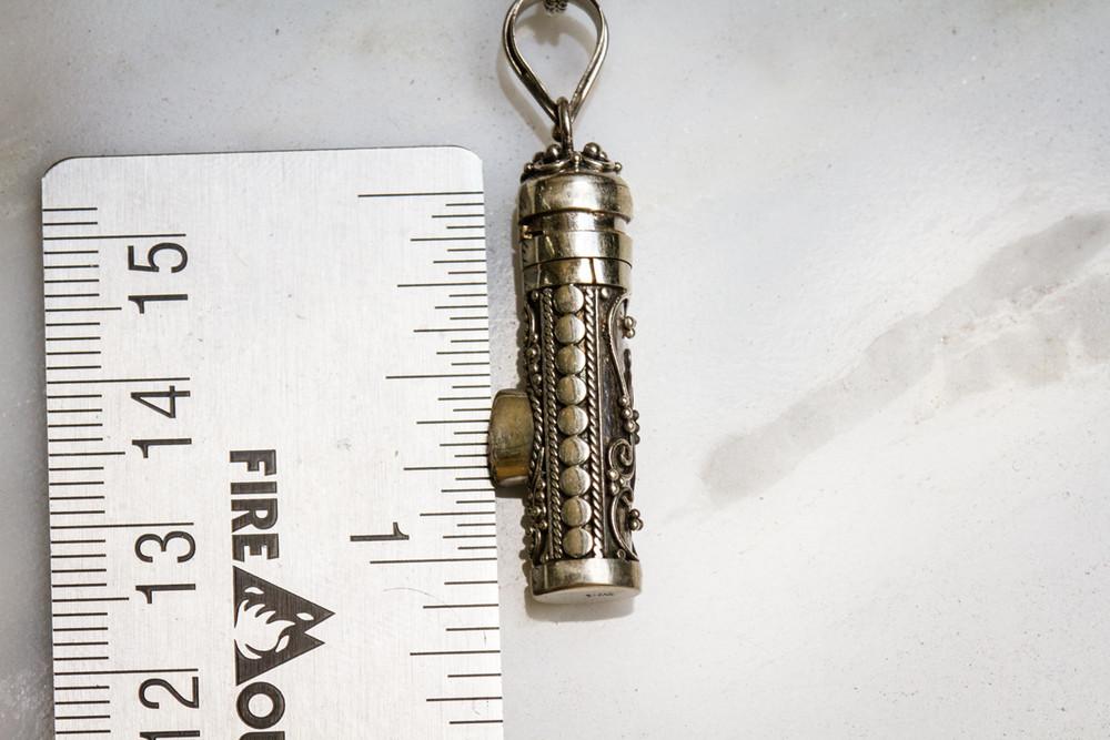 Sterling silver keepsake urn pendant with a small gem inset and twist off top for cremains or hair, shown with a ruler for scale