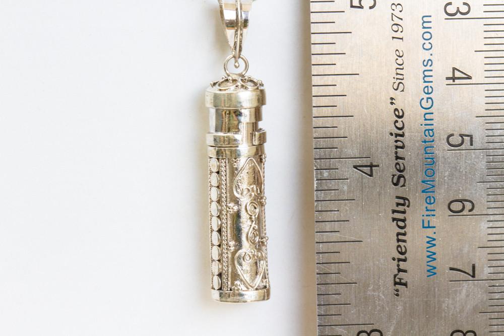 Double heart filigree sterling silver keepsake pendant with a twist off top for cremains or hair, shown beside a ruler for scale