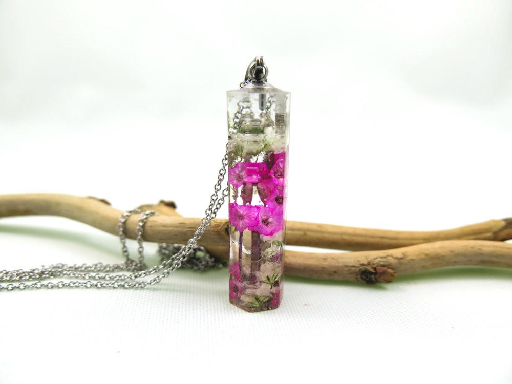 Close up of crystal resin pendant with pink blooms suspended inside on a stainless steel chain.