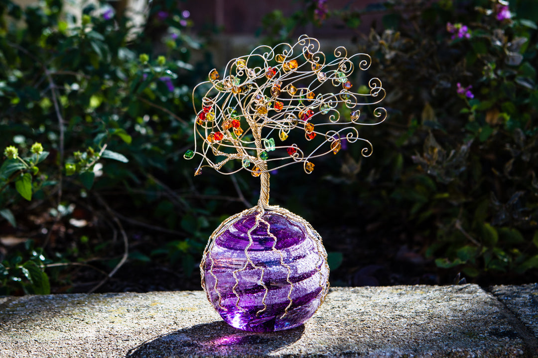 Golden Tree of Life sculpture perched on a purple glass orb outdoors