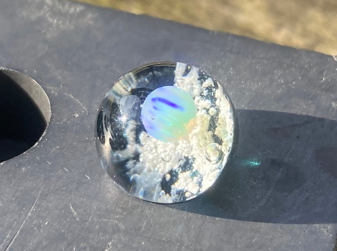 Clear marble with a blue iridescent opal center encased in cremation ashes