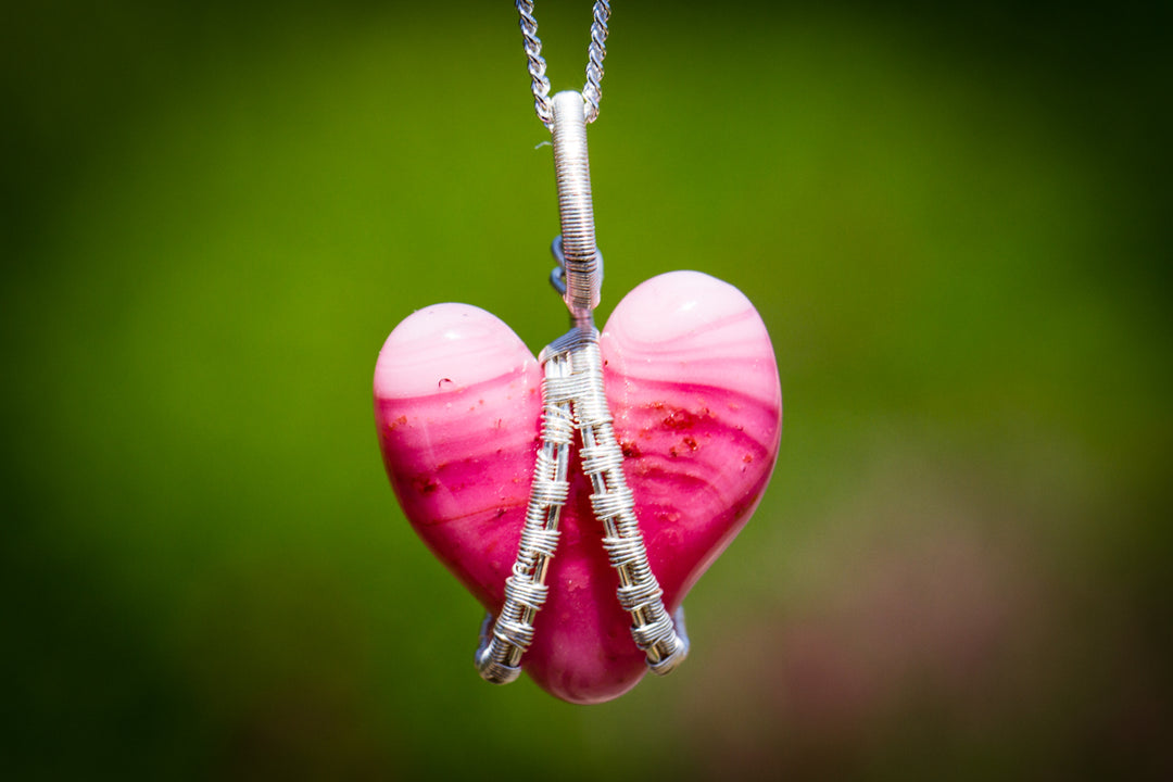 Pink glass heart pendant wrapped in silver wire hanging from a silver chain.